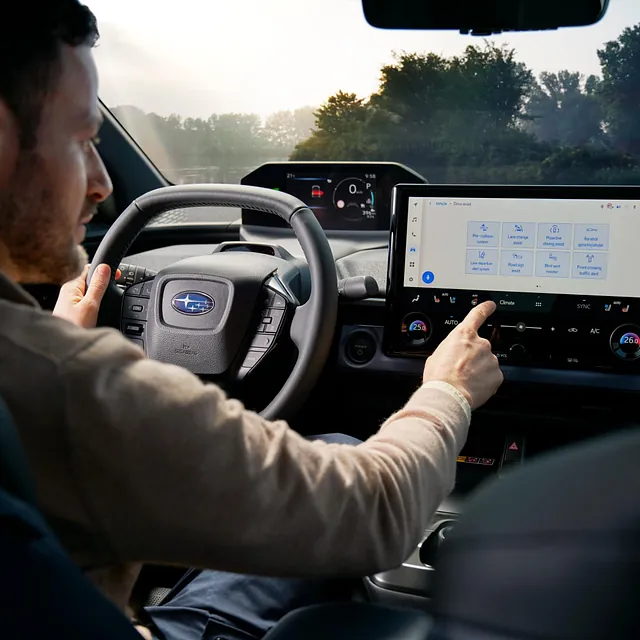Fører justerer berøringsskjerm i moderne førermiljø med stort digitalt instrumentpanel.
