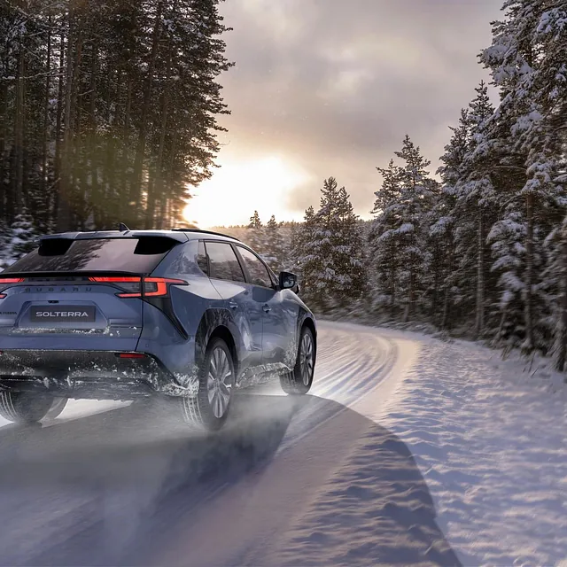 Subaru Solterra på snødekt vei i skogen, vinterlandskap og sol bak trærne.